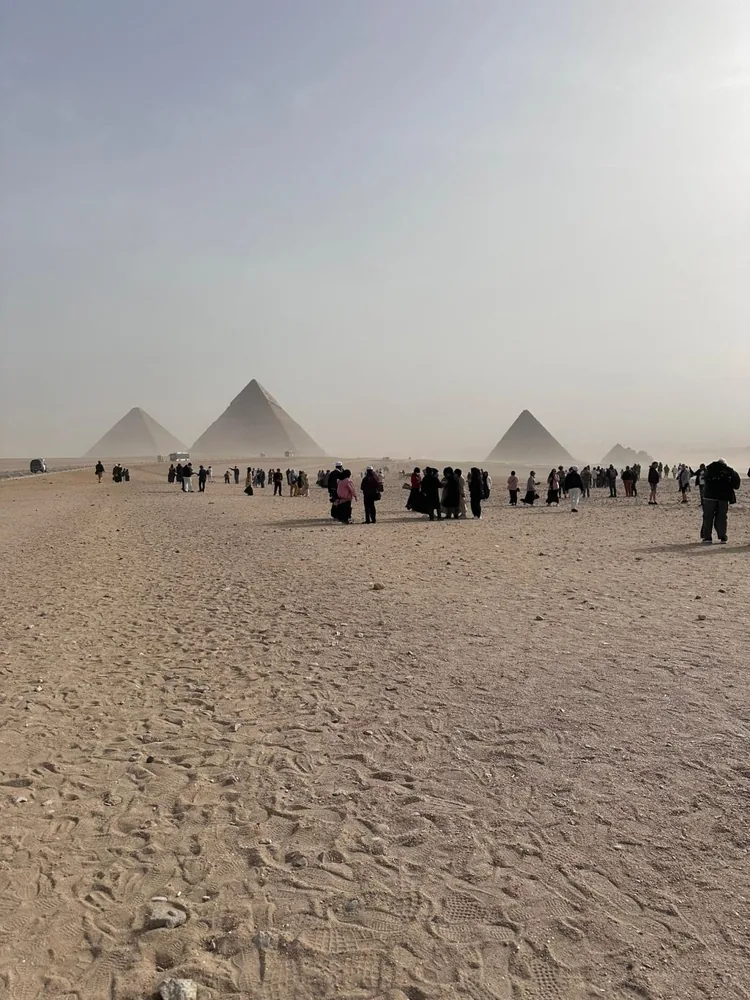 Crowds of visitors walking on the sand towards the pyramids on a hazy morning